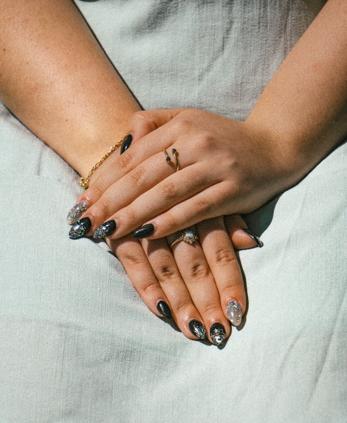 Close-up of hands with black and silver nail art wearing rings, bathed in sunlight.