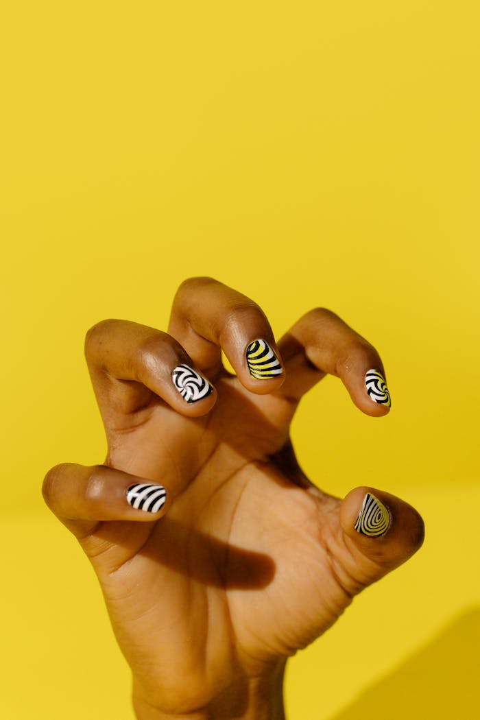 Close-up of a hand with artistic swirl nail designs on a bright yellow background.