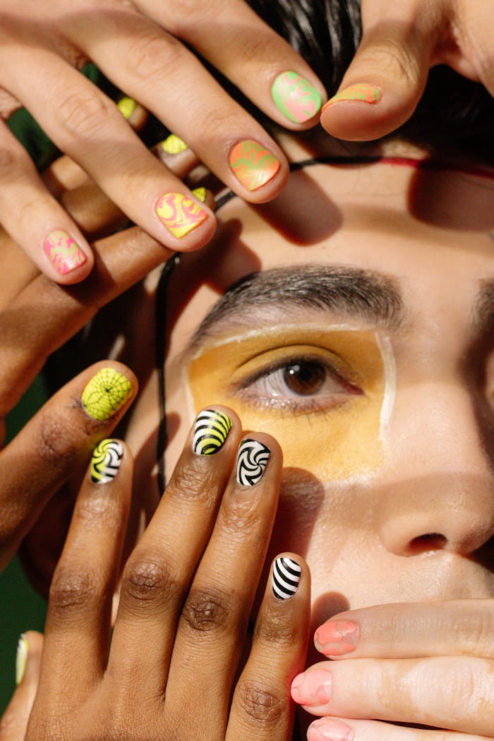 A vibrant close-up photo showcasing diverse nail art designs on hands framing a face.